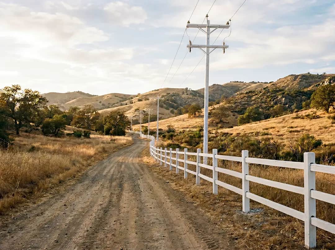 Wooden fence along a dirt road with utility poles, set against a hilly landscape, illustrating infrastructure resilience in wildfire-prone areas, relevant to NanoTech Materials' protective coating applications.